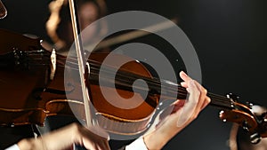 Women bows over the strings of a violin in a room. Black background. Close up