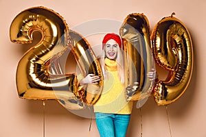 Women celebrating New Year xmas party happy laughing in yellow sweater blouse with 2019 gold balloons