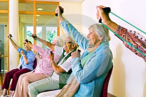 Women in chairs using stretching bands.