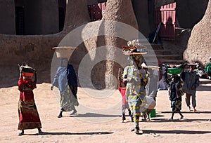 Women and children carry market goods on their heads, walking past the Great Mosque of Djenne, Mali