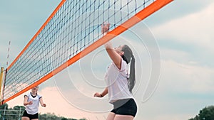 Women competing in a professional beach volleyball tournament. A defender attempts to stop a shot during the 2 women