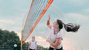Women competing in a professional beach volleyball tournament. A defender attempts to stop a shot during the 2 women