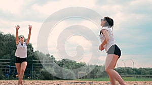 Women competing in a professional beach volleyball tournament. A defender attempts to stop a shot during the 2 women