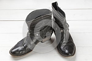 Women cowboy boot. Black leather shoes on a white wooden table. Composition of clothes. Flatlay