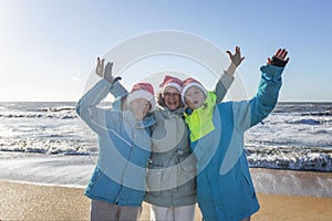 Women of different ages in Santa hats on the seashore on a sunny day in winter. Celebrating New Year and Christmas