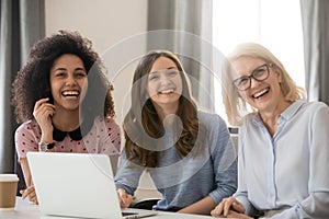 Women different ethnicity and ages looking away laughing at workplace photo