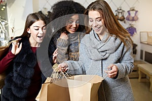 Women of diverse ethnicity with shopping bags posing in clothing store. Portrait of three smiling multiracial girls