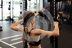 Women doing pull ups training arms with trx fitness straps in the gym. Upper body training. Back view.