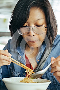 Women eating egg noodle with crispy pork from chopsticks and met