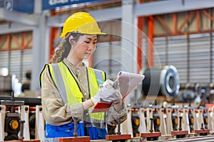 Women engineer take notes on paperwork quality control standing at machine of factory warehouse