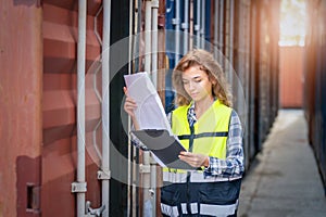 Women Engineer wears PPE checking container storage with cargo container background at sunset. Logistics global import or export