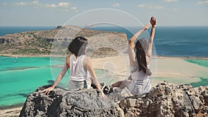 Women enjoying their holidays. Silhouette of two young girls standing on cliff with the view on blue sea lagoon holding