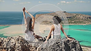 Women enjoying their holidays. Silhouette of two young girls standing on cliff with the view on blue sea lagoon holding