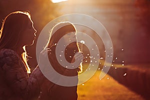 Women freedom and hope. Nature and harmony. Romantic sunset. Two young women taking and blowing a dandelion flower. Warm lighting