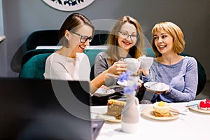 Women friends looking at cakes, three girl friends drinking coffee in the cafe and eating desserts, women during lunch