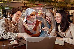 Women. Friends Meeting In Cafe. Four Smiling Girls Sitting In Restaurant With Laptop And Tablet. Diversity Female Working