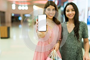 Women friends showing the smartphone screen while shopping