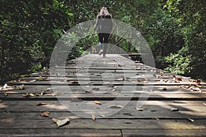 Women or girl walking alone on wooden track in forest