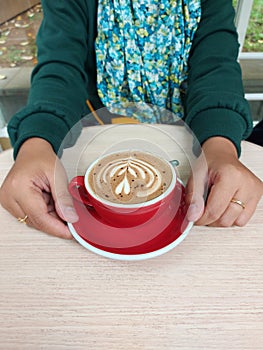 Women hand hold cup of coffee latte art on the wooden table. Isolated background. Coffee time concept