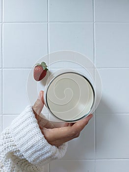 Women hand hold a glass of milk. Completed with a storawberry. Bright mood photogtaphy. Flat lay technique. Isolated background.