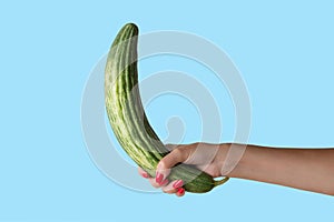 Women hand holding cucumber like a man`s penis on blue background. Erotic concept