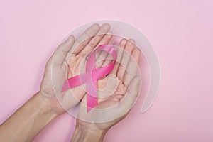 Women hand holding pink ribbon breast cancer on pink background.