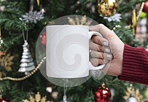 Women hand holding white ceramic coffee cup on christmas tree background. mockup for creative advertising text message or