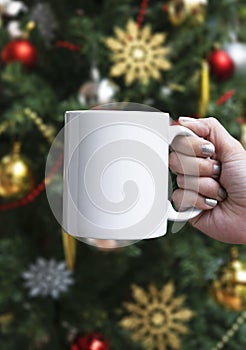 Women hand holding white ceramic coffee cup on christmas tree background. mockup for creative advertising text message or