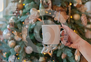 women hand holding white ceramic coffee cup on christmas tree background. mockup for creative advertising text message