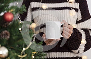 Women hand holding white ceramic coffee cup with christmas tree background. mockup mug for creative advertising text message or