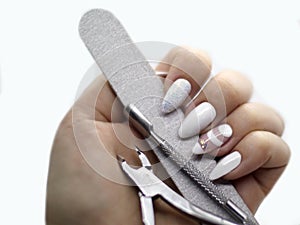 Manicure tools - pusher, cuticle nipper and buffer in hand with long white nails