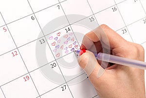 Women hand with pencil drawing hearts shape in calendar for Valentines day