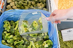 Women hand pick up frozen broccoli in supermarket