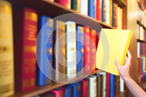 Women hand pulling yellow book from wood bookshelves in public library. Colorful books, Textbook, Literature on bookshelf.