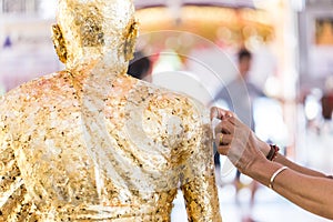 Women hand putting gold leaf onto The Buddha statue to gild. photo