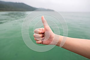 Women hand with thumb up on green sea