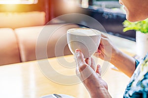 Women hands holding hot cup of coffee or tea in morning sunlight