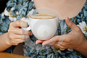 Women hands holding hot cup of coffee or tea in morning sunlight