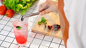 Women hands prepairing mocktail by putting sweet mulberry into a glass with an iced pink color drink