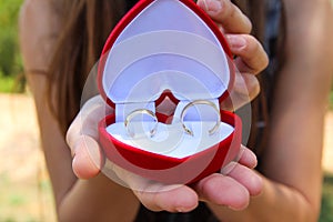 Women hands with a velvet red box with a pair of gold wedding rings