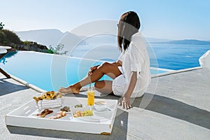 Women having breakfast by the infinity pool looking out over the Caldera ocean of Santorini Greece
