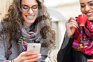 Women having coffee and looking at pictures on smart phone