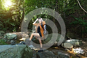 Women hiker with backpack checks map to find directions and look binoculars in wilderness area at waterfalls and forest.