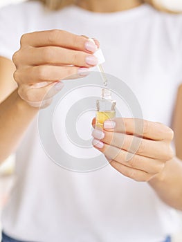 Women hold an opened dropper bottle with cosmetic oil. Wear a white t-shirt. Place for your logo