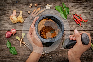 The Women hold pestle with mortar and spice red curry paste ingredient of thai popular food on rustic wooden background. Spices i