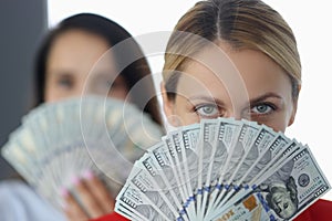 Women are holding fan of one hundred dollar bills.