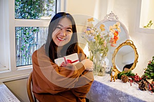 Women holding gift box smiling and happy at home with Christmas home decoration on background