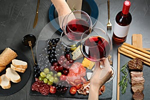 Women holding glasses of red wine over table with snacks