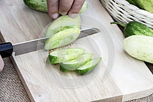 Women holding knife cutting slices raw cucumber fresh on wooden cutting board on sackcloth background for cooking ingredient in