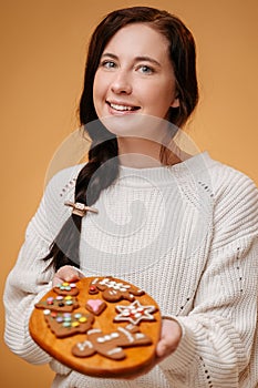 Women holding a wooden board with gingerbread on a yellow background.